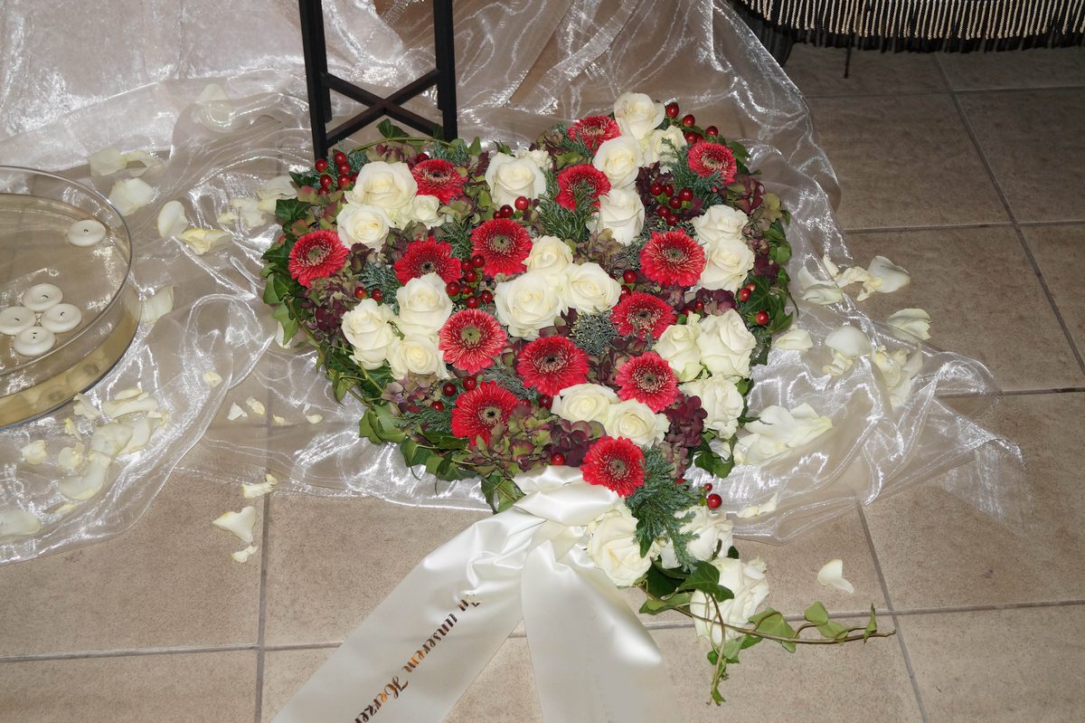 Liegendes Blütenherz aus roten Gerbera und weißen Rosen mit Schleife