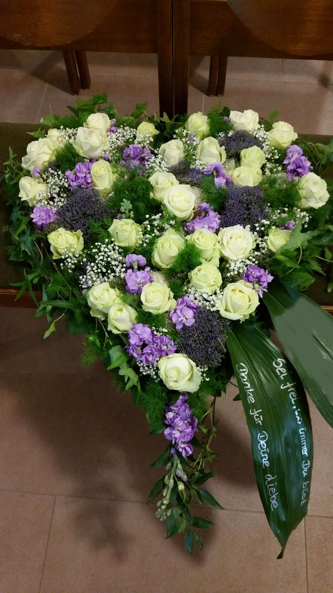 Herz aus weißen Rosen und violetten Blüten mit heller Schleife