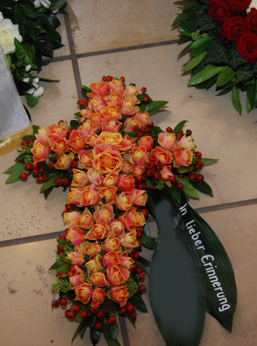 Kreuz aus apricotfarbenen Rosen mit Schleife und der Aufschrift In lieber Erinnerung