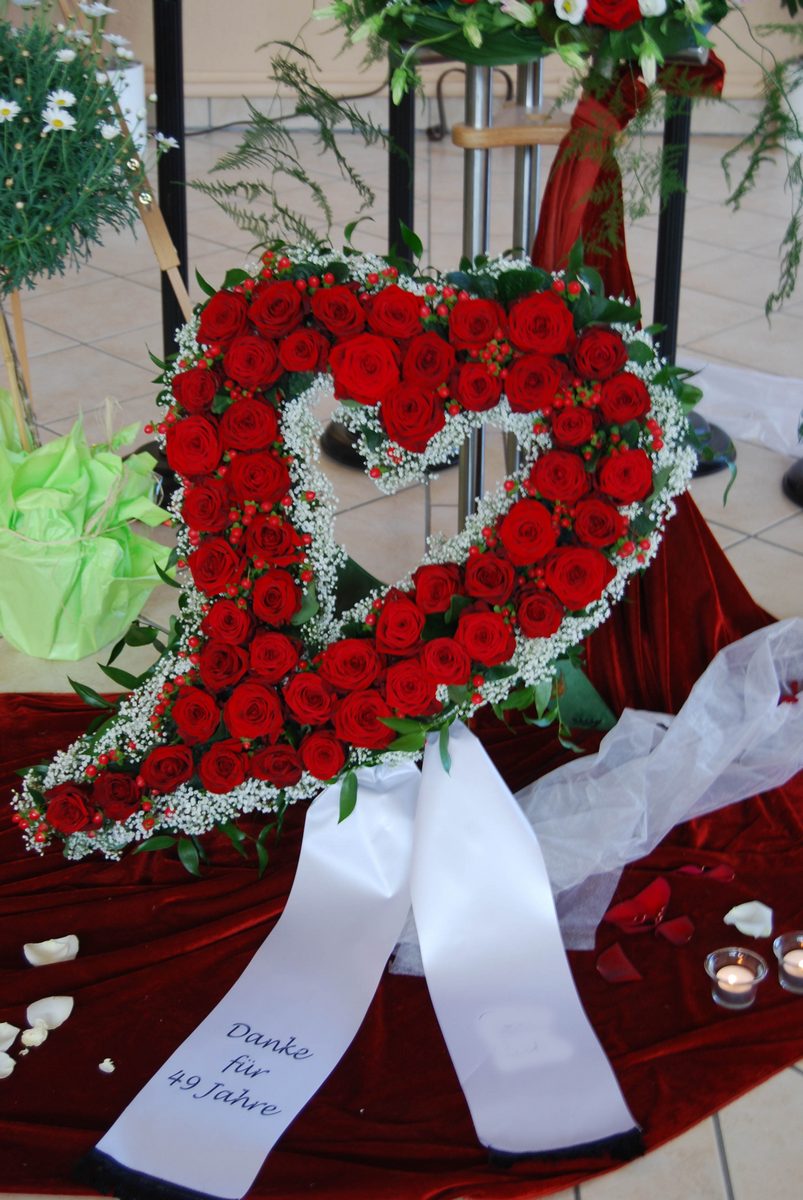 Aufrechtes Herz aus roten Rosen mit weißen Schleierblüten und beschrifteter Schleife