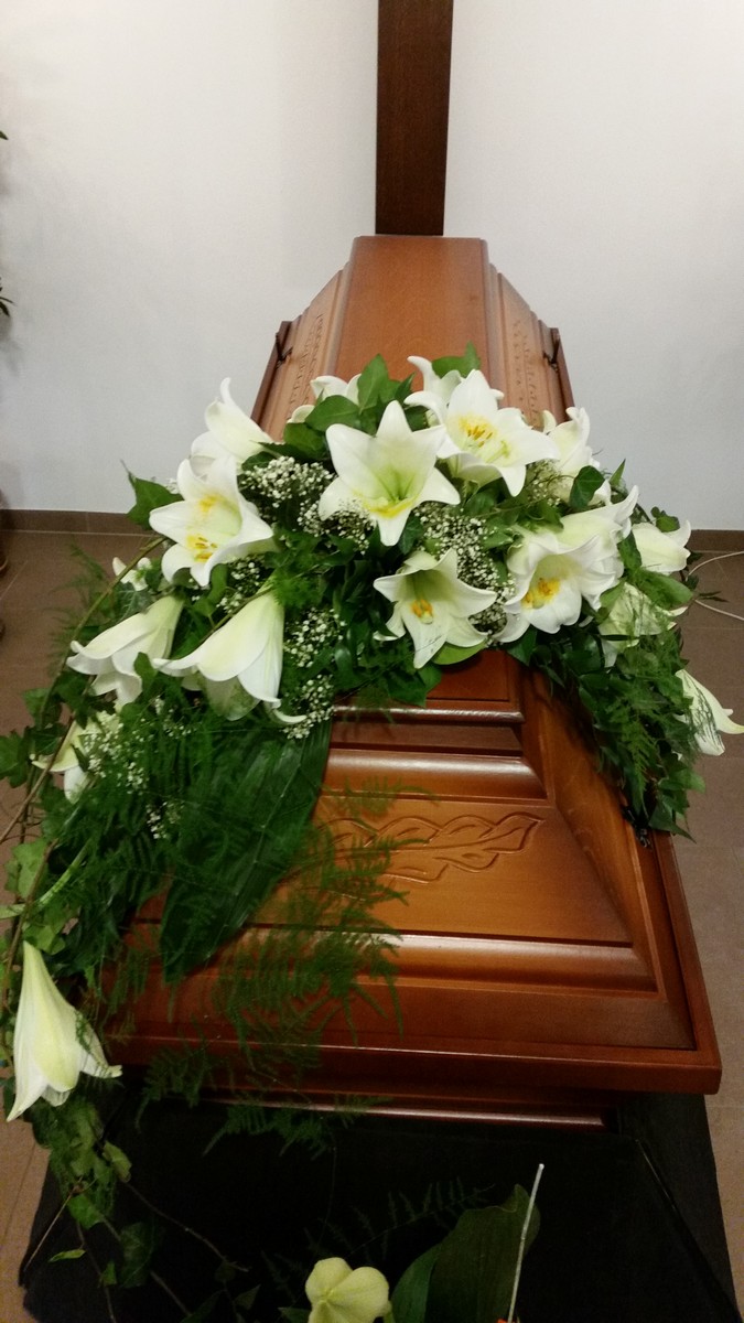 Sarg aus dunklem Holz mit weißem Sargbukett aus Lilien und Amaryllis