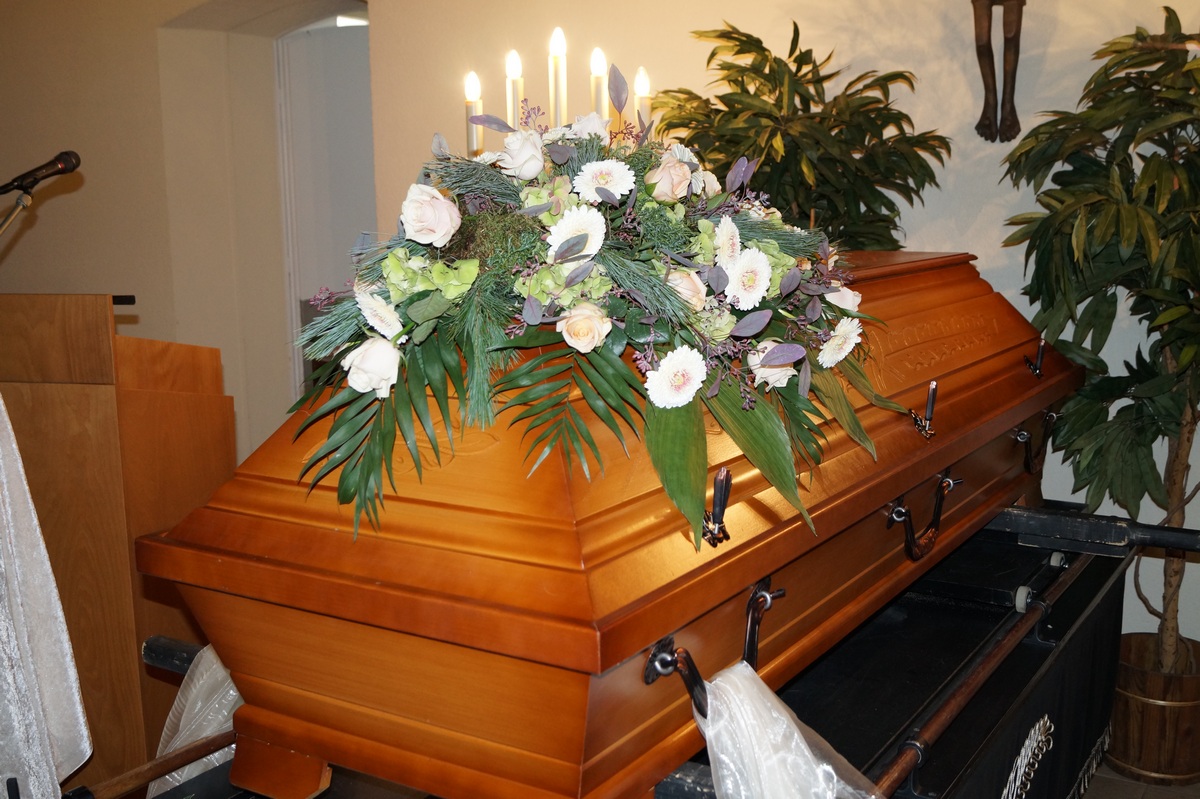 Sarg mit Sargbukett in Weiß und Creme, Kerzen im Hintergrund