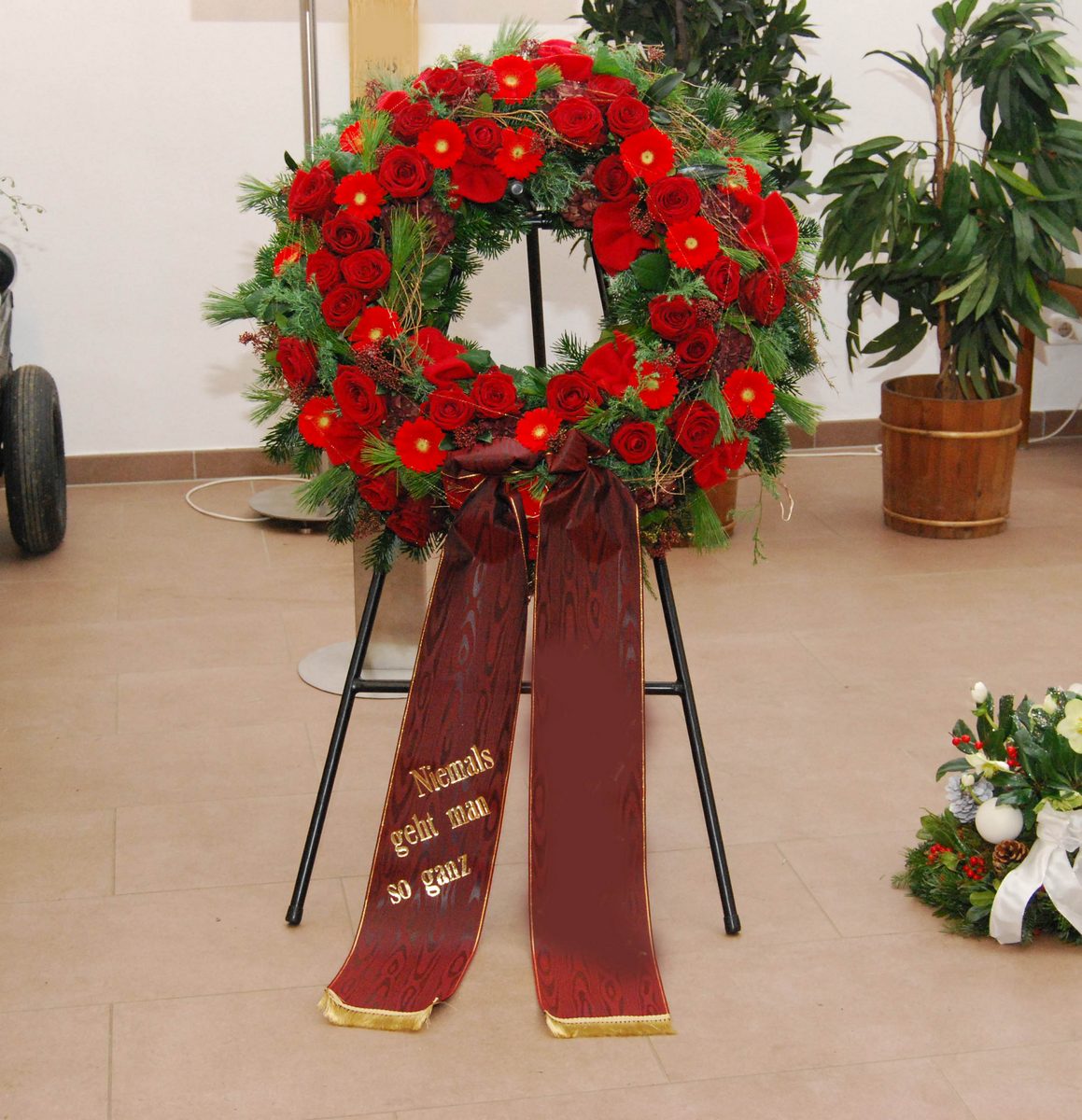 Runder Trauerkranz aus roten Rosen auf einem Ständer, mit dunkelroter Schleife