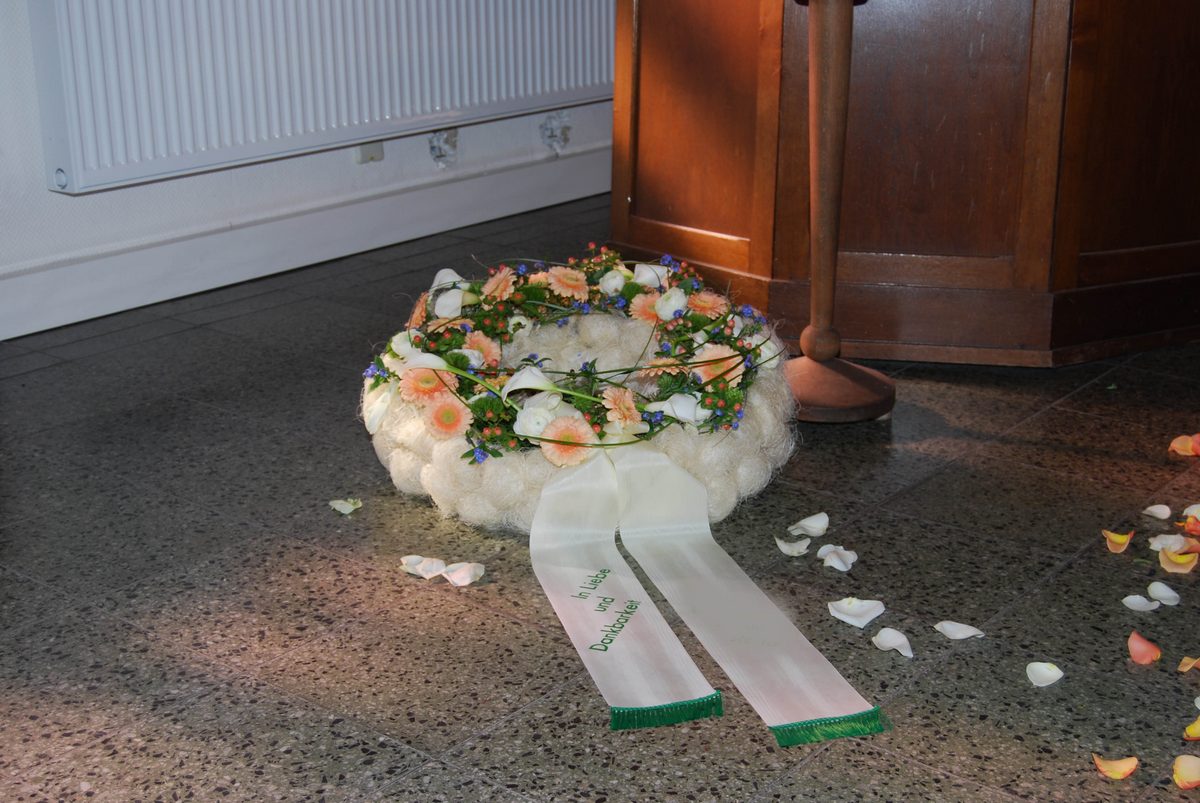 Liegender Trauerkranz in Weiß und Apricot mit Schleifen und gestreuten Rosenblättern