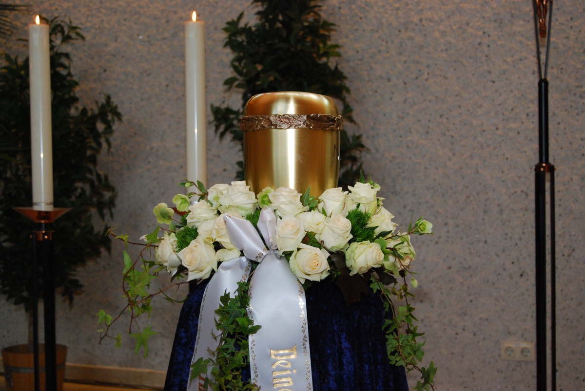 Goldene Urne auf einem Podest mit weißem Rosenschmuck und Efeu, Kerzen daneben