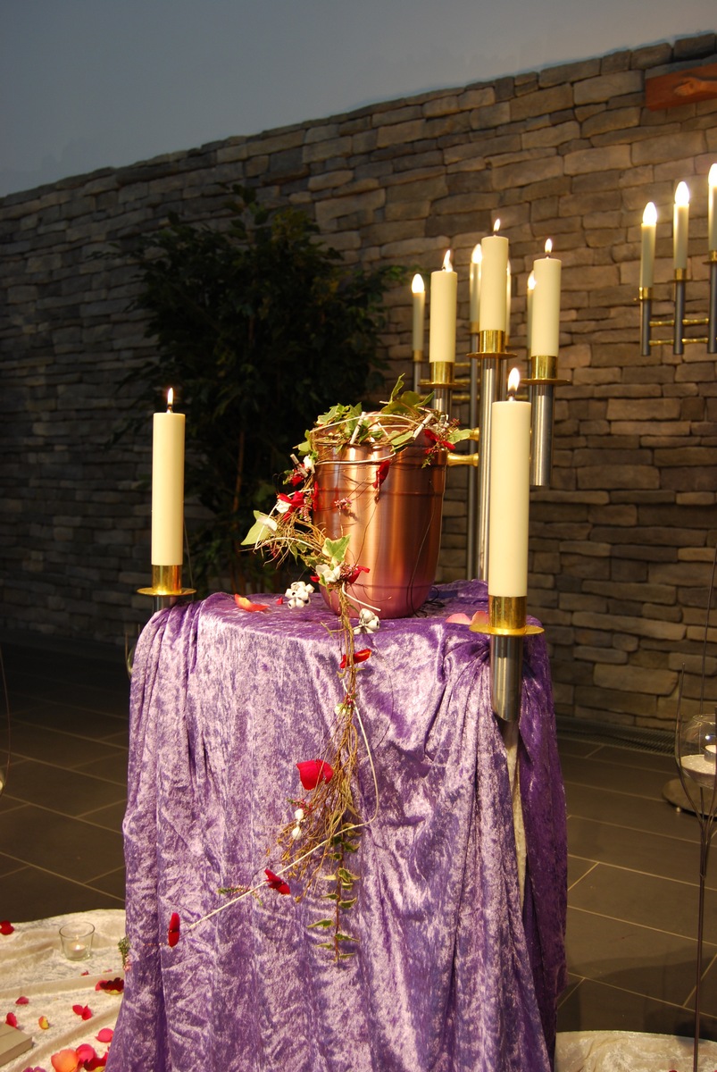Kupferfarbene Urne auf violettem Tuch mit Rankenschmuck und Kerzenleuchtern
